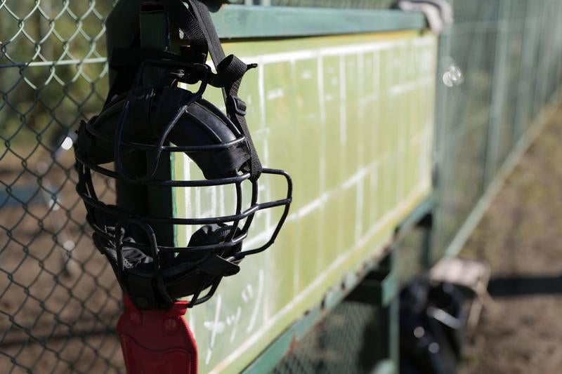 野球場のベンチに掛けられた黒いキャッチャーマスクの写真