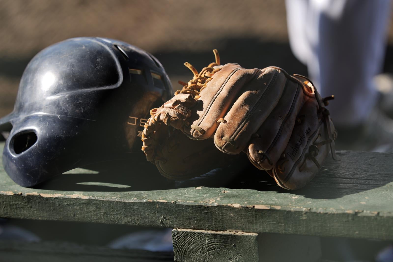 木製ベンチの上に置かれた黒い野球ヘルメットと茶色のグローブ
