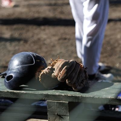 少年野球場のベンチに置かれたバッティングヘルメットとグローブの写真