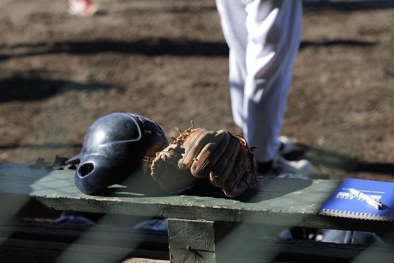 少年野球場のベンチに置かれたバッティングヘルメットとグローブの写真