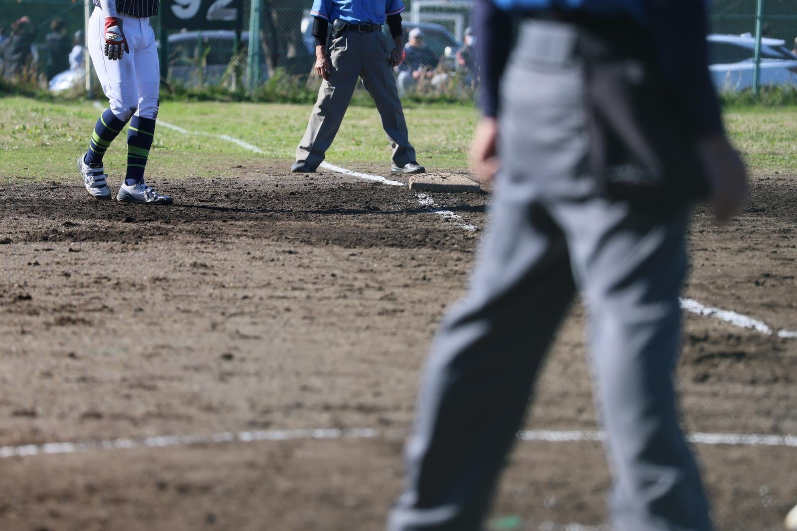 土のグラウンドで行われている野球の試合で審判と選手が写っている
