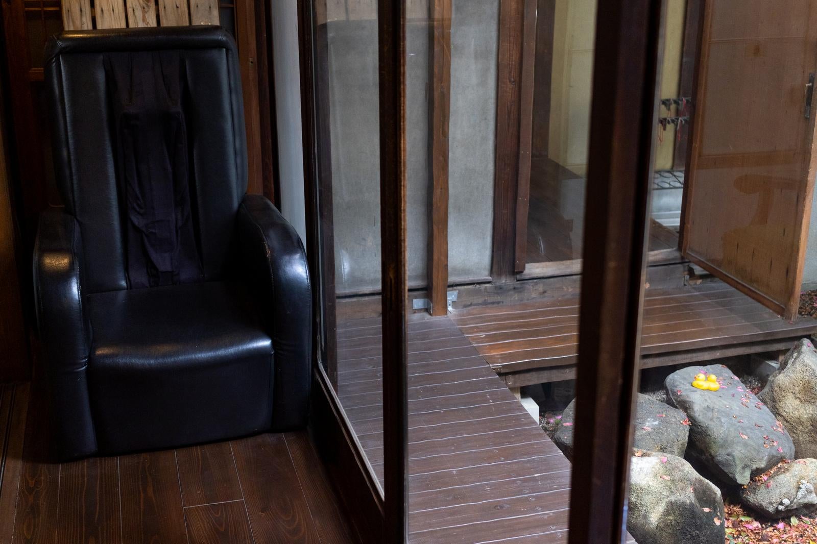 古民家の縁側に置かれた黒い革張りのマッサージチェアとガラス戸越しに見える石庭