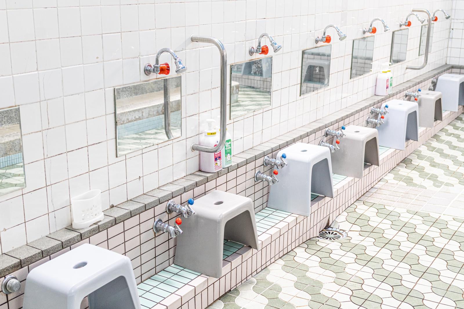 銭湯の洗い場に蛇口と風呂椅子、鏡が横一列に並ぶ様子