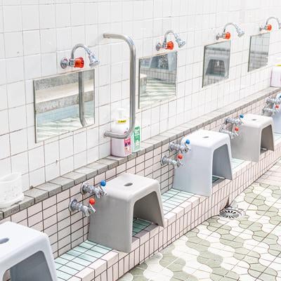 銭湯の洗い場に並ぶ蛇口と風呂椅子の写真