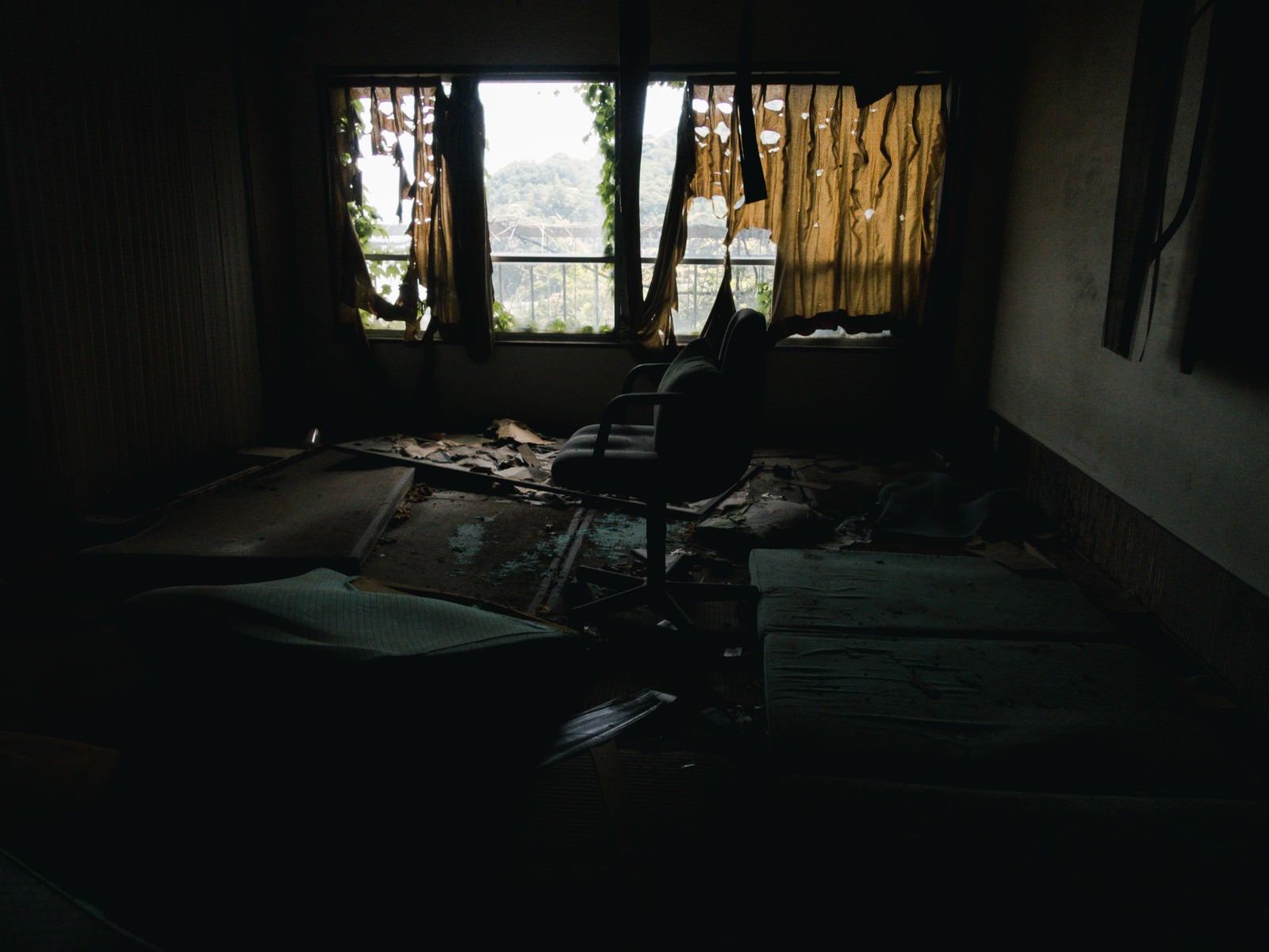 「カーテンの隙間から照らされる瓦礫まみれの椅子」の写真