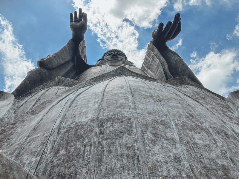 天空に向かって両手をあげる牛久大仏の姿の写真