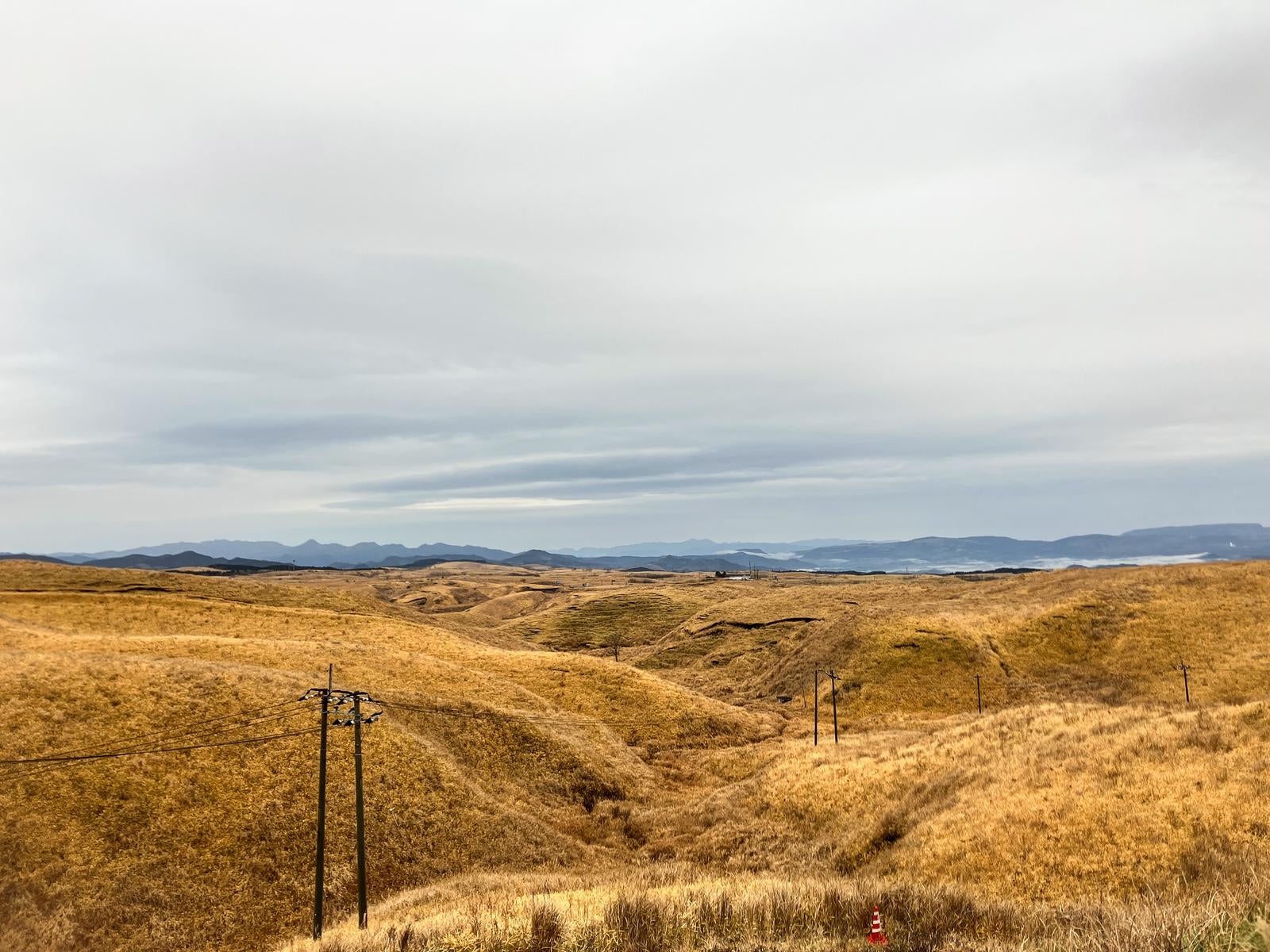 曇天の空の下、大観峰に広がる枯れ草の丘陵と遠くの山並み