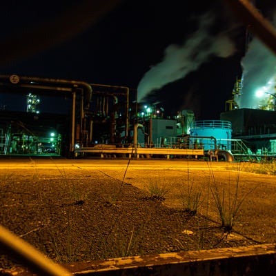 フェンス越しに見る工場の夜景の写真