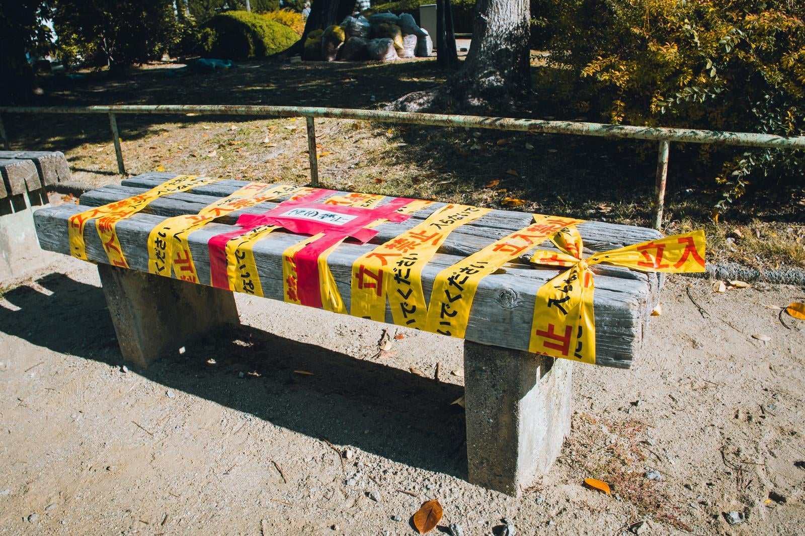 立入禁止と書かれた黄色いテープが何重にも巻かれた公園の木製ベンチ