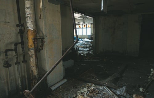 床に散らばった瓦礫とぶら下がる錆び付いた配管の写真