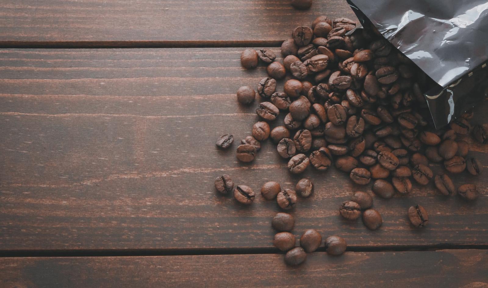 黒いパッケージから流れ出した焙煎コーヒー豆が木製テーブルの上に散らばっている