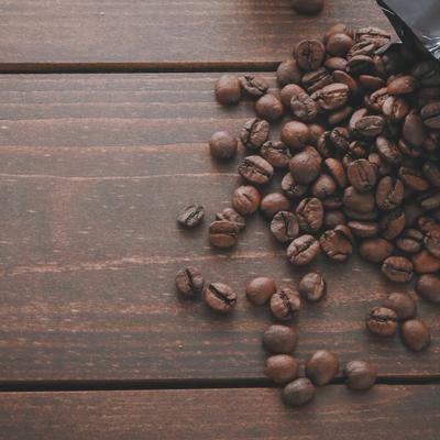 黒いパッケージから溢れる焙煎したコーヒー豆が散らばる木製テーブルの写真