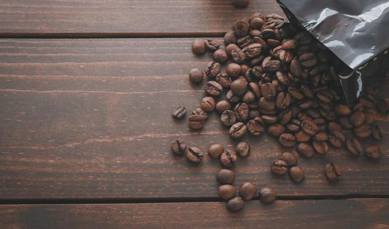 黒いパッケージから溢れる焙煎したコーヒー豆が散らばる木製テーブル