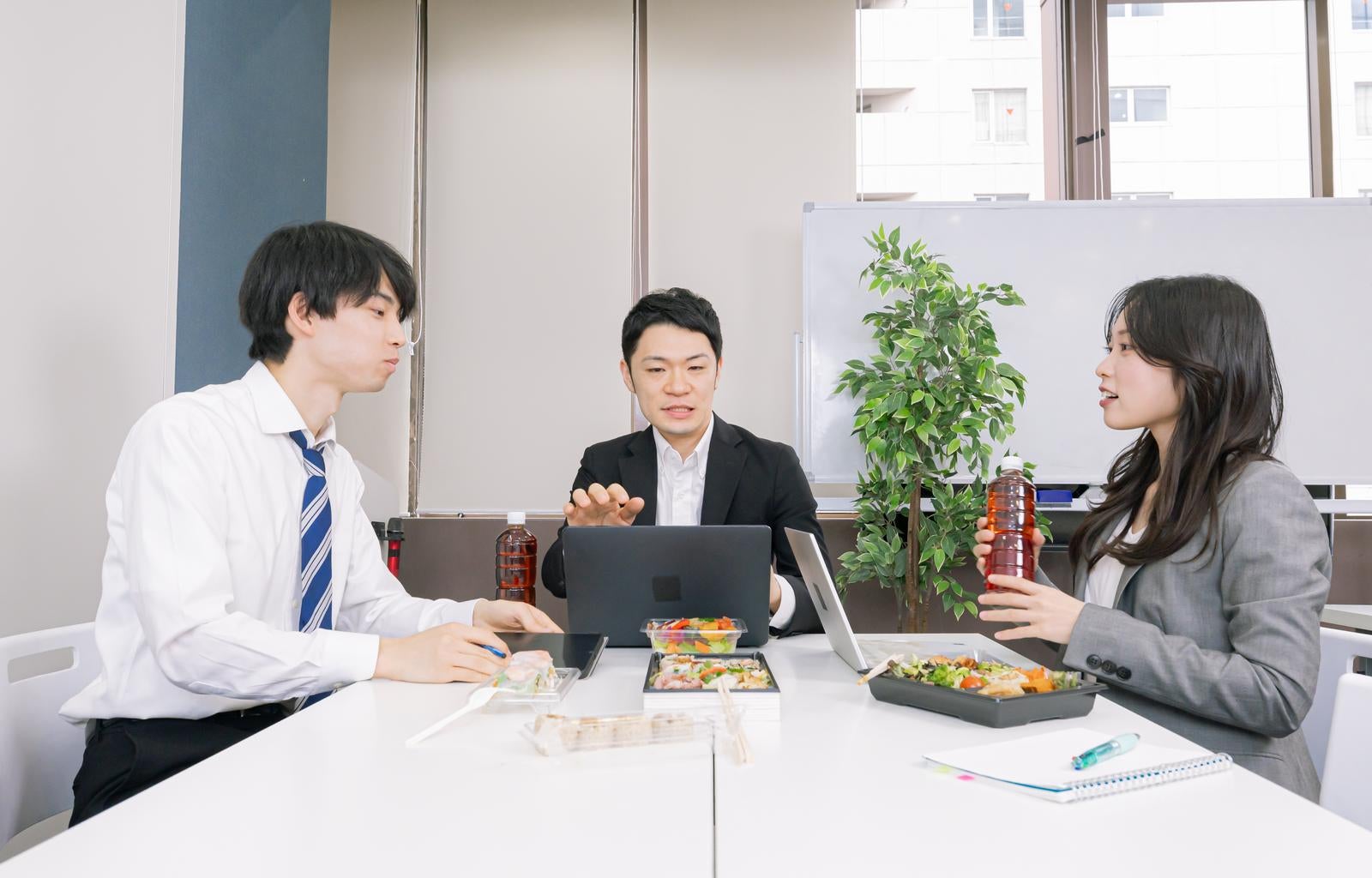 「昼食を取りながら会議するビジネスマンたち」の写真［モデル：たくみ 吉屋ゆり モデルリリース］