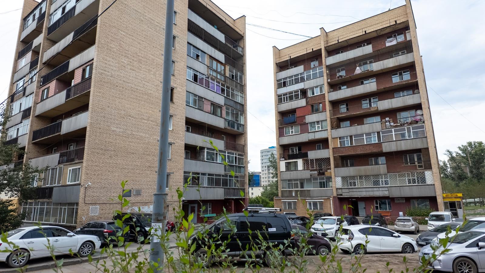 ウランバートルに建つレンガ造りの集合住宅2棟と手前の駐車場に停まる車