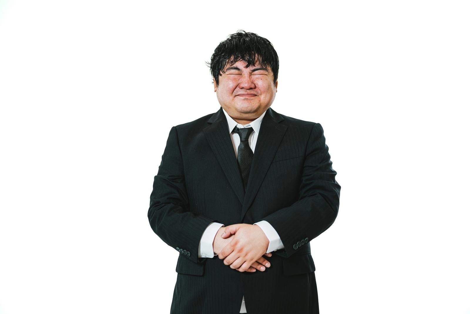 A man in a black suit with clasped hands striking a welcoming hospitality pose (omotenashi)