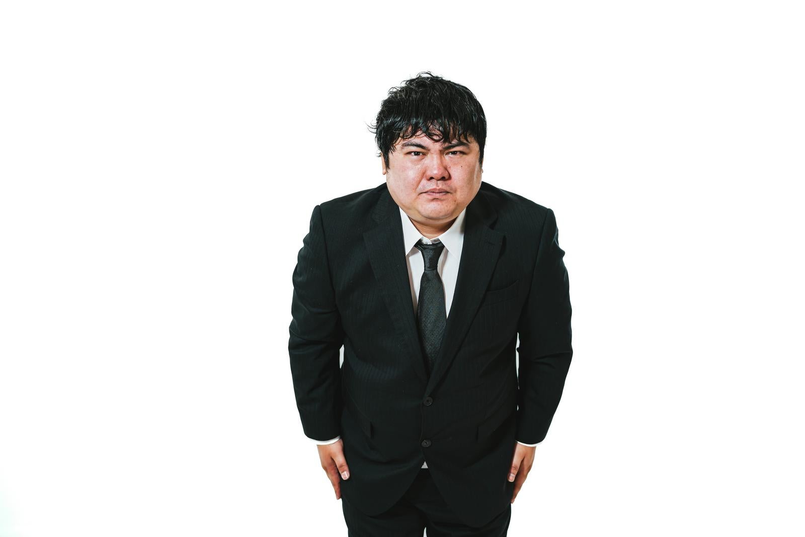 黒いスーツを着た男性が両手を下げて謝罪している［モデル：段田隼人］