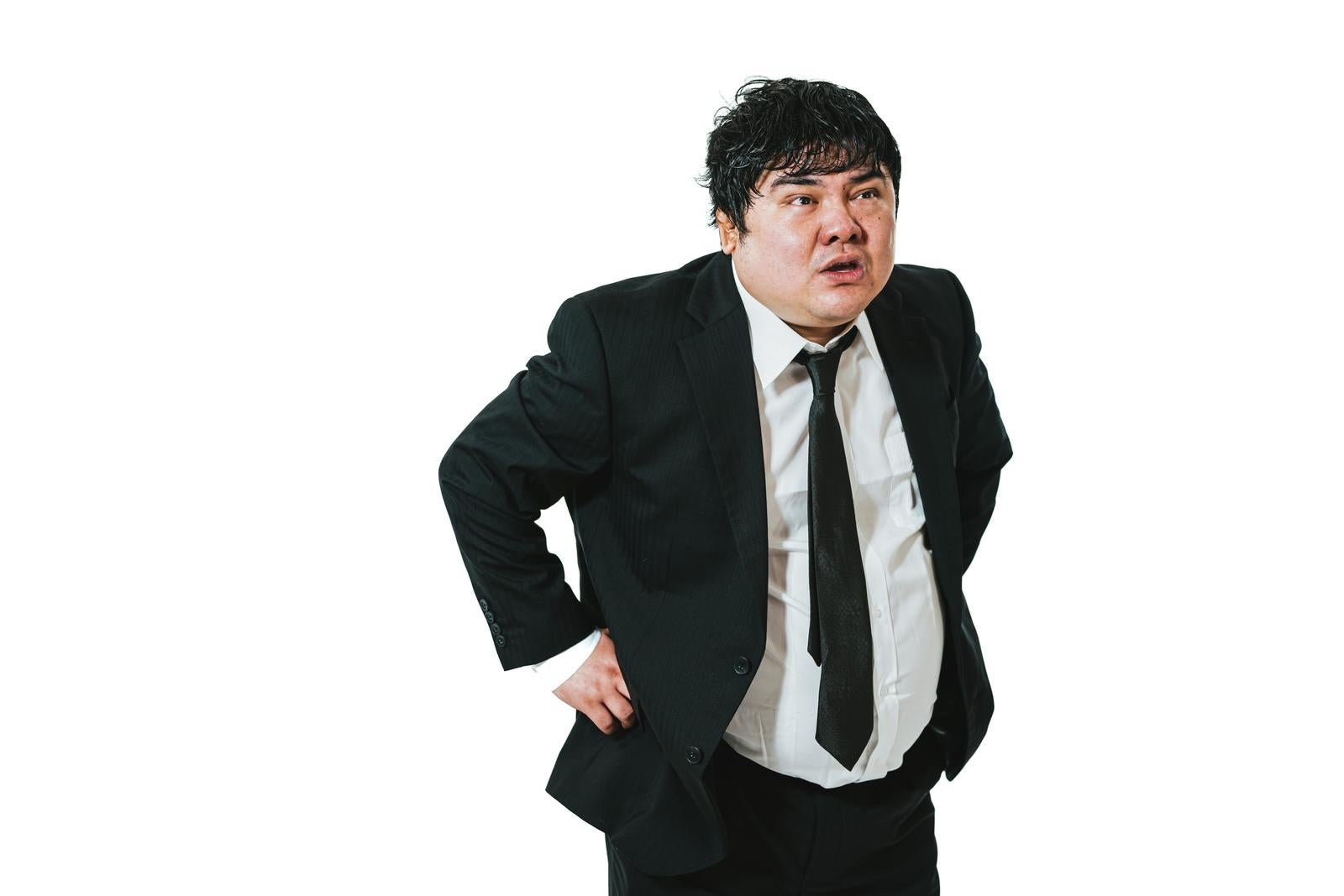Overweight businessman in suit leaning forward with hand on lower back, out of breath in front of white background