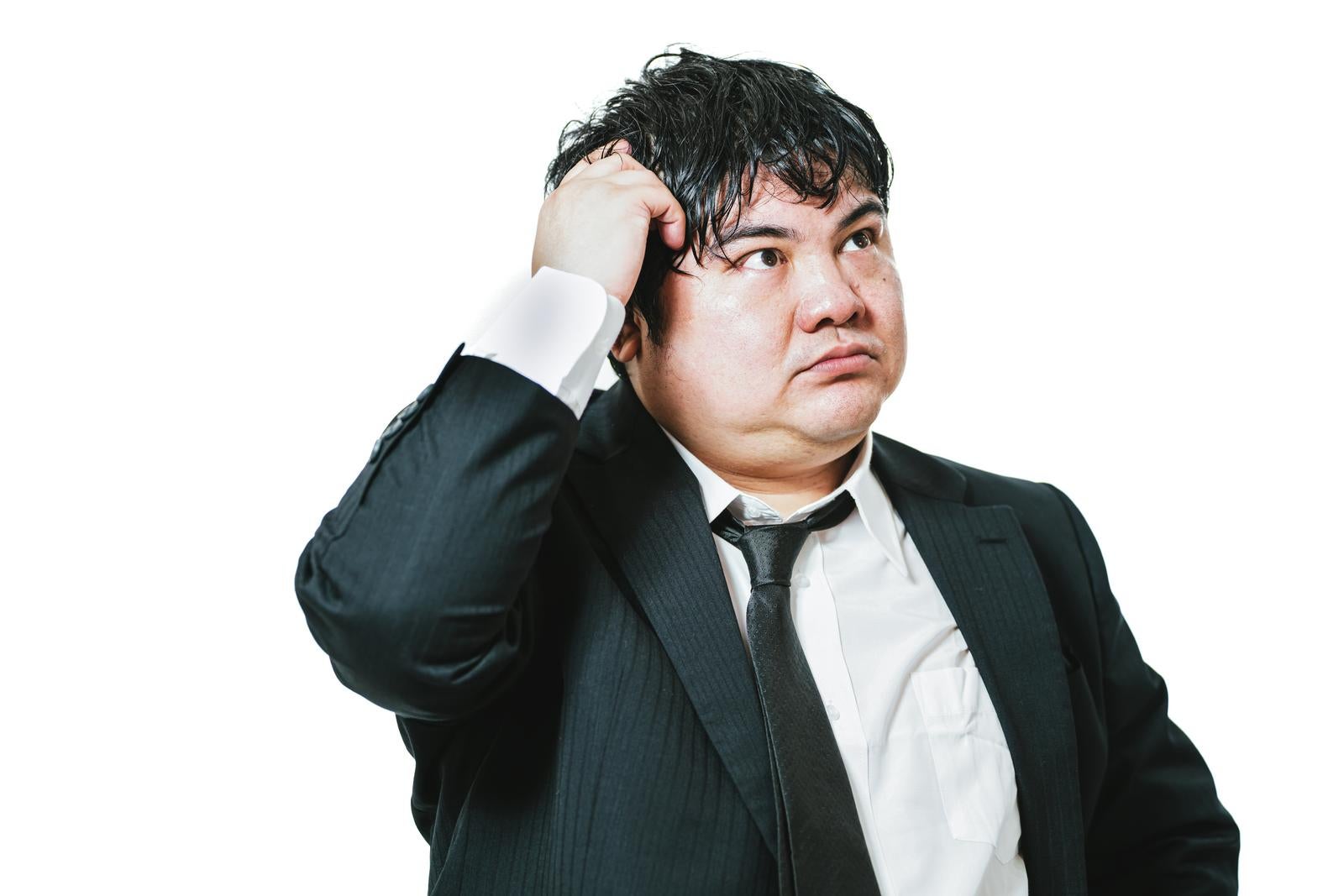 Male businessman in suit scratching his head with his right hand with a troubled expression looking upward against a white background