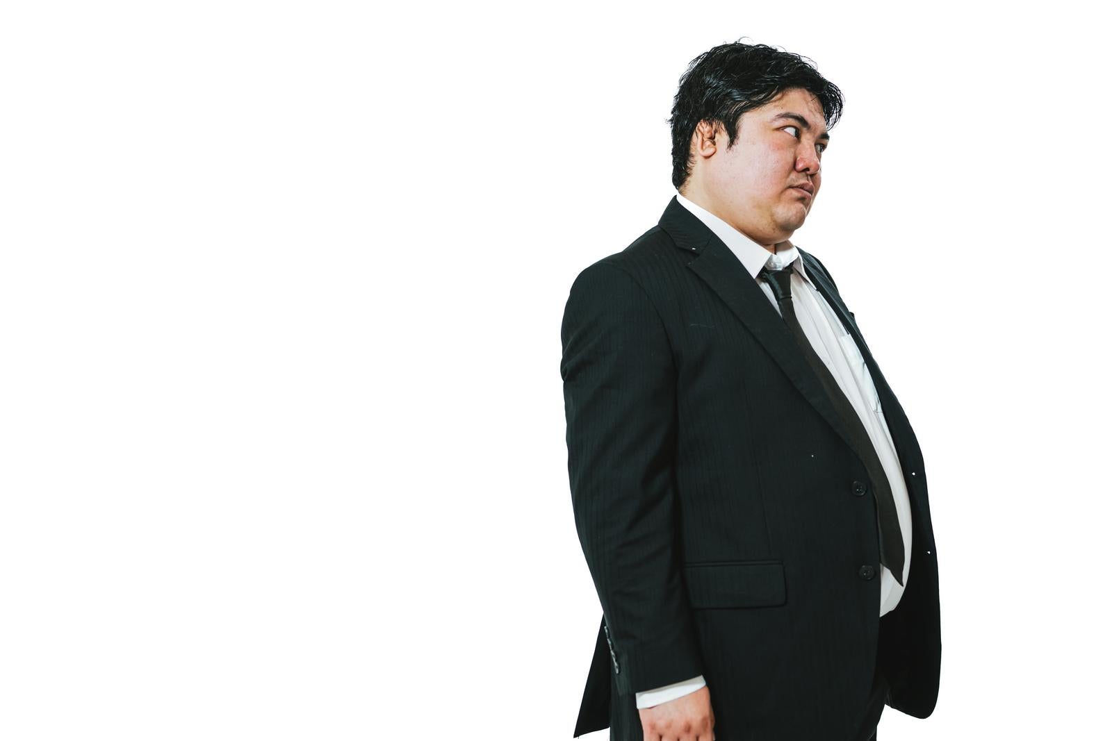 An overweight man in a suit with a displeased expression in profile against a white background