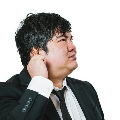 首に手を当てて悩むスーツ姿の会社員の写真