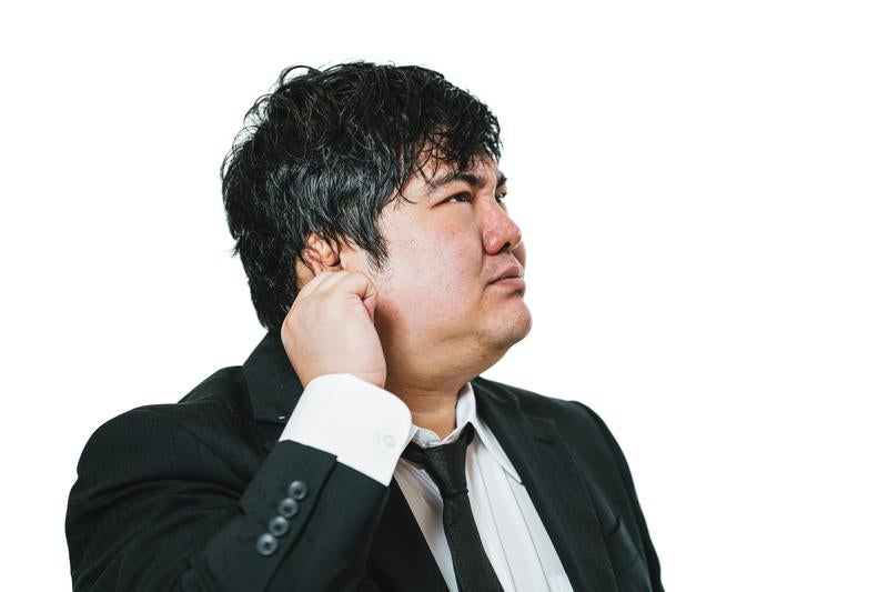 首に手を当てて悩むスーツ姿の会社員の写真