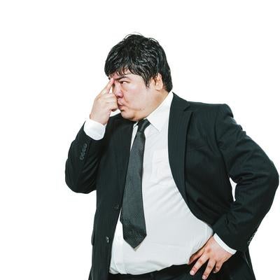 鼻をつまんで考え込むスーツの男性の写真