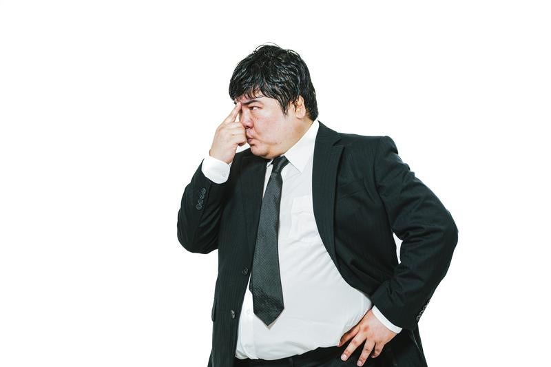 鼻をつまんで考え込むスーツの男性の写真