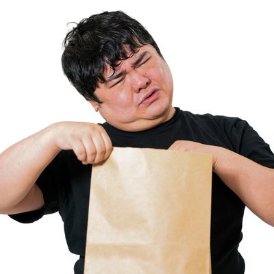 茶色い紙袋を両手で持ち、目をつむって中身を確認しようとする男性の写真