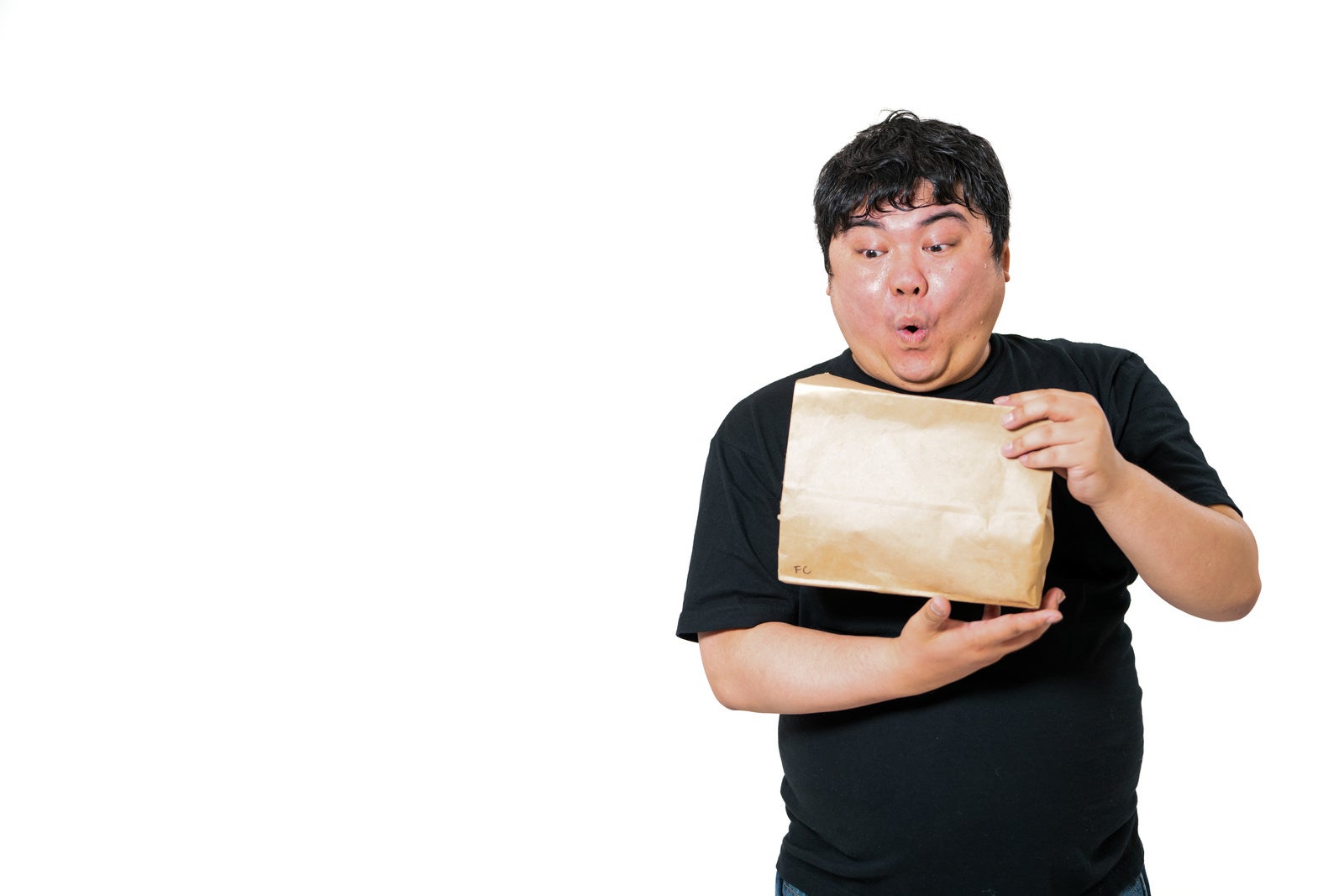 黒いTシャツを着た男性が茶色い紙袋を開けて驚いている［モデル：段田隼人］