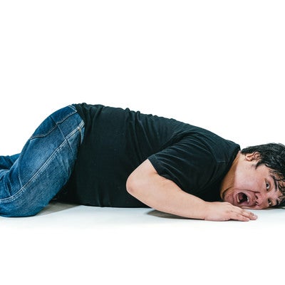 床に伏せて苦しむ表情の男性の写真