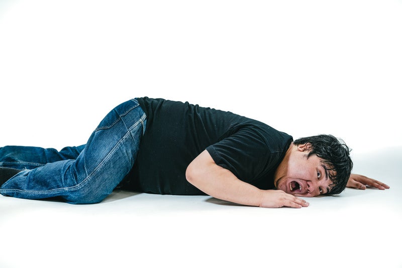 床に伏せて苦しむ表情の男性の写真