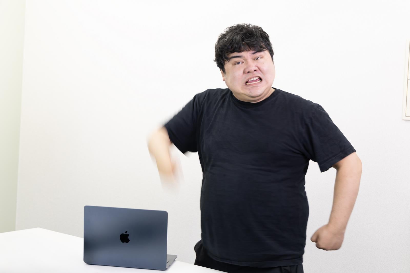 「腕を振り下ろしてPCに怒りや苛立ちを叩く男性」の写真［モデル：段田隼人］