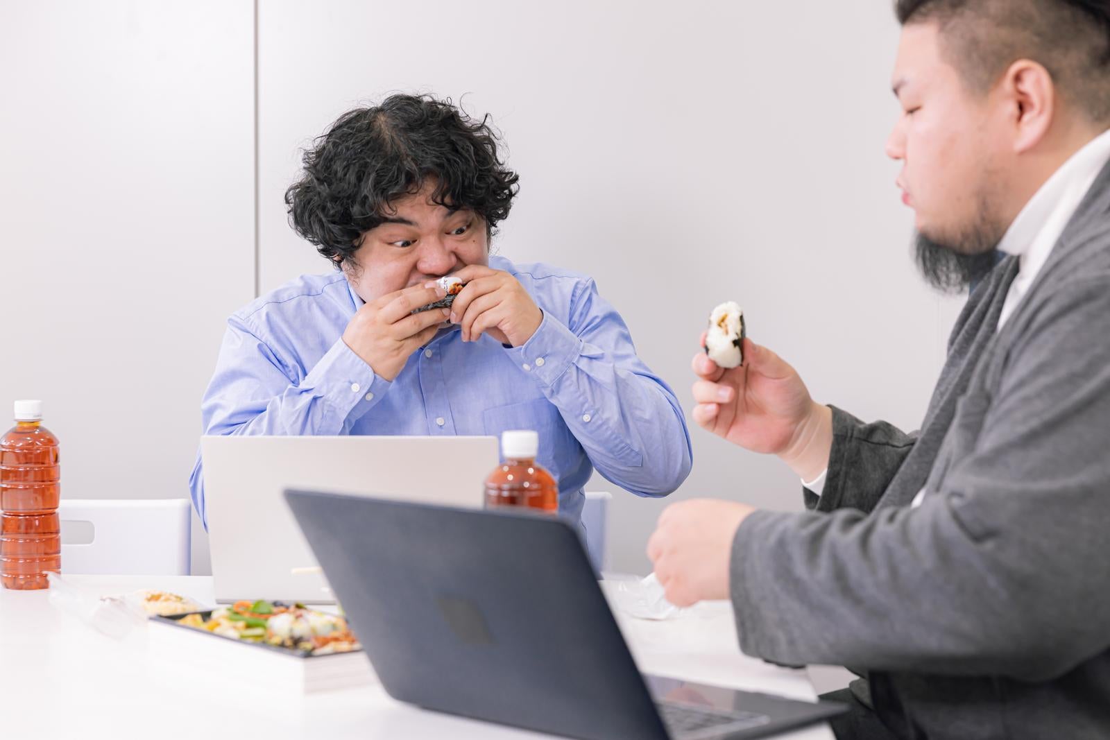 「時短で飯を食べながら打ち合わせするエンジニア」の写真［モデル：段田隼人 うまみん］