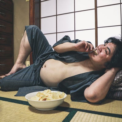 腹を出してポテチを食べながら寝転ぶ昭和男子の写真