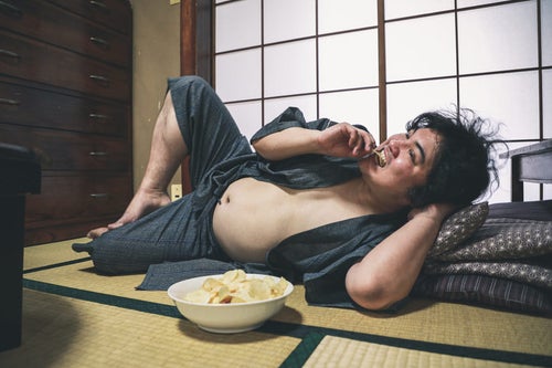 腹を出してポテチを食べながら寝転ぶ昭和男子の写真