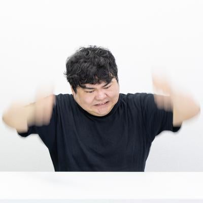 男性が机の前で両腕を大きく振り上げている瞬間の写真