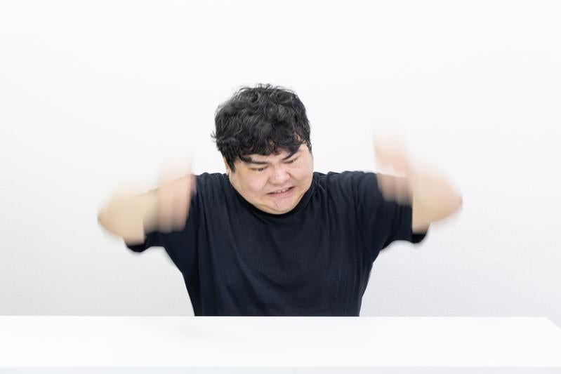 男性が机の前で両腕を大きく振り上げている瞬間の写真