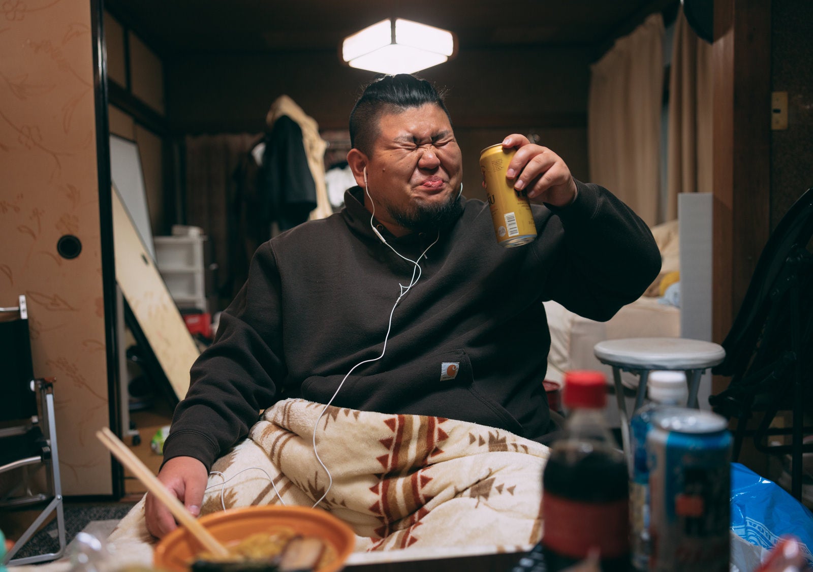 「イヤホンを付けて缶ビールを飲むデブ男子」の写真［モデル：ノリックス］