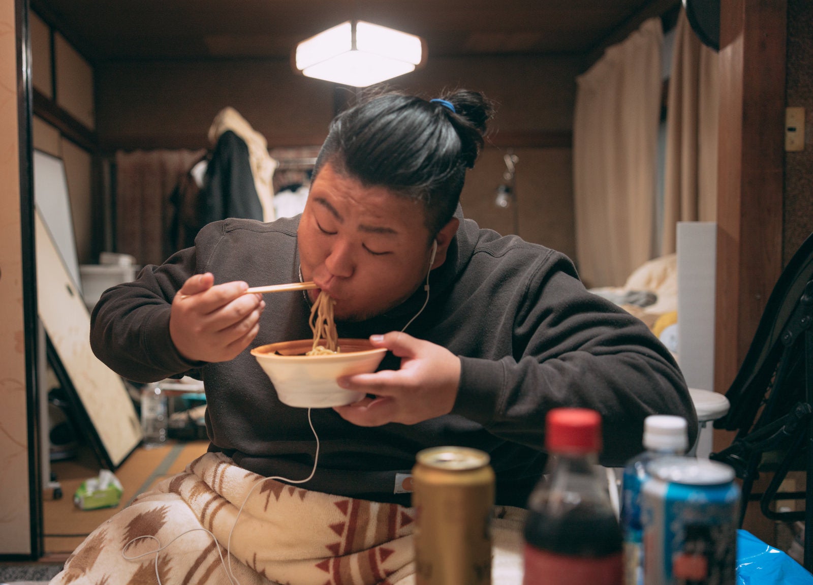「散らかった部屋でラーメンを食べる肥満男子」の写真［モデル：ノリックス］