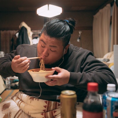 散らかった部屋でラーメンを食べる肥満男子の写真