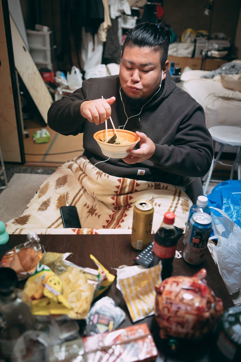 コタツに入りながらラーメンを食す無精髭の男性の写真