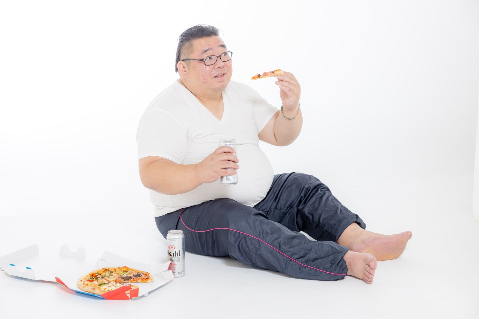 「缶ビール片手にピザを食す膨よかな男性」の写真［モデル：ダルマ親方］