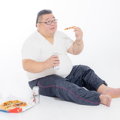 缶ビール片手にピザを食す膨よかな男性の写真