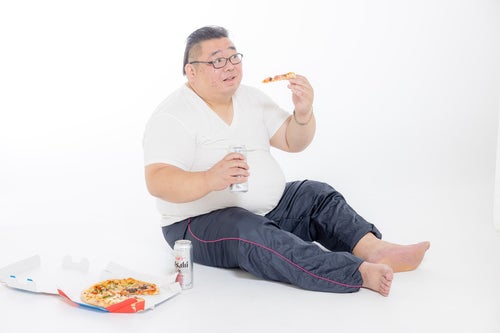 缶ビール片手にピザを食す膨よかな男性の写真