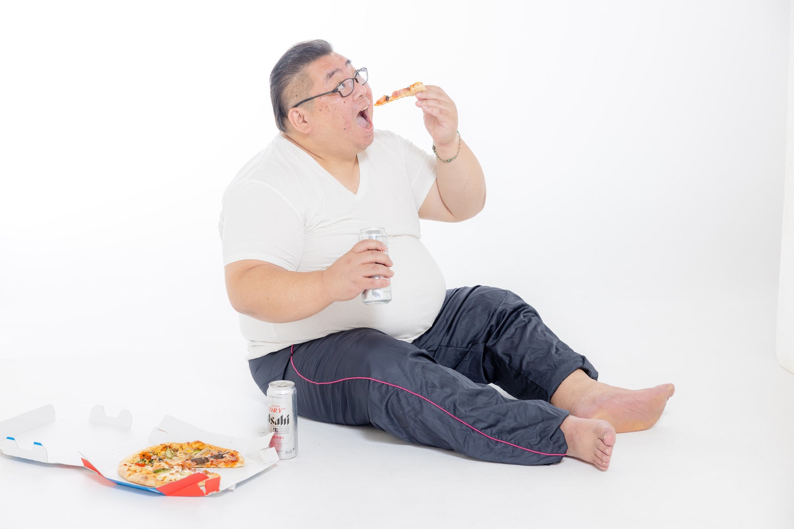 「大きな口でピザを食す膨よかな男性」の写真［モデル：ダルマ親方］