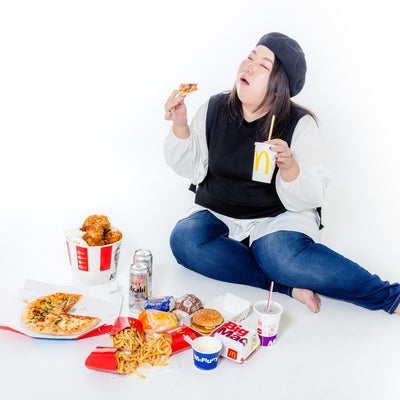 ファーストフードに囲まれた白い床でジャンクフードを食べる女性の写真