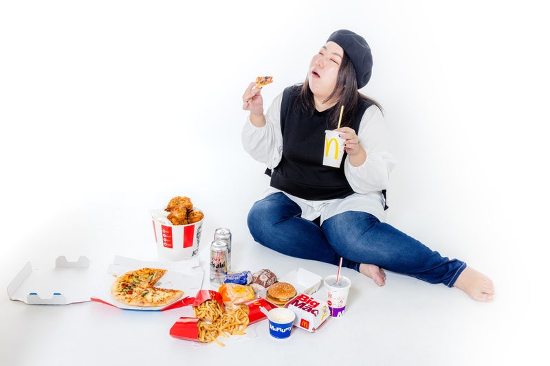 ファーストフードに囲まれた白い床でジャンクフードを食べる女性の写真
