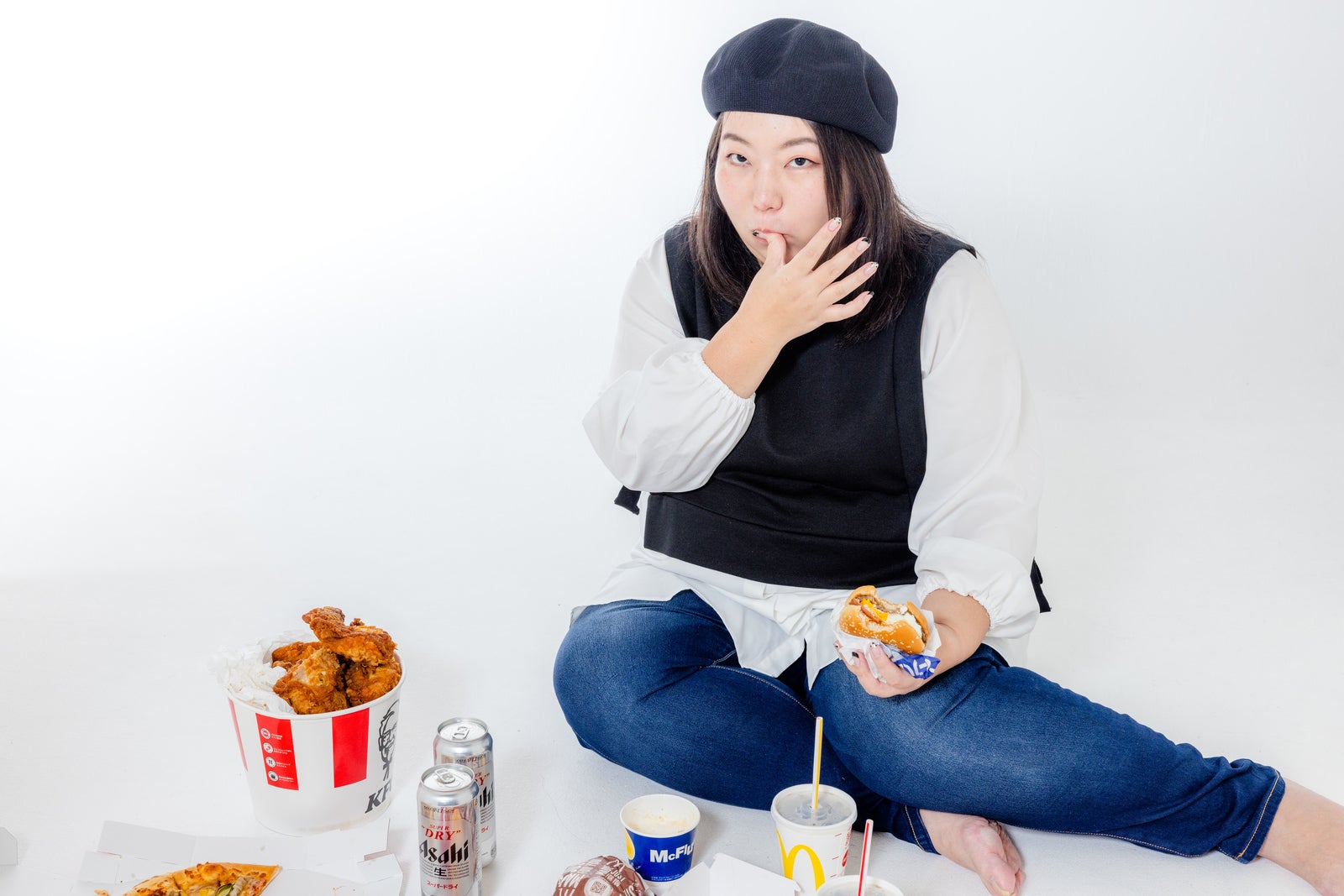 「指を舐めるジャンクフードを食す女性」の写真［モデル：KANA］