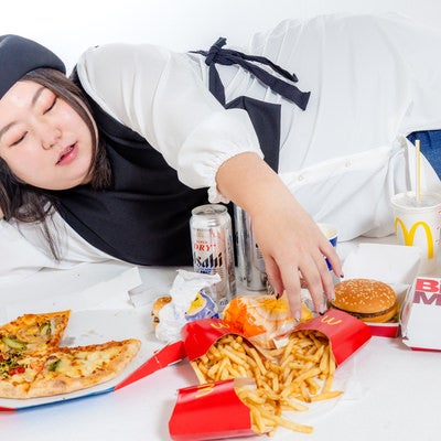 白いテーブルに広げたジャンクフードを前に横たわる女性の写真